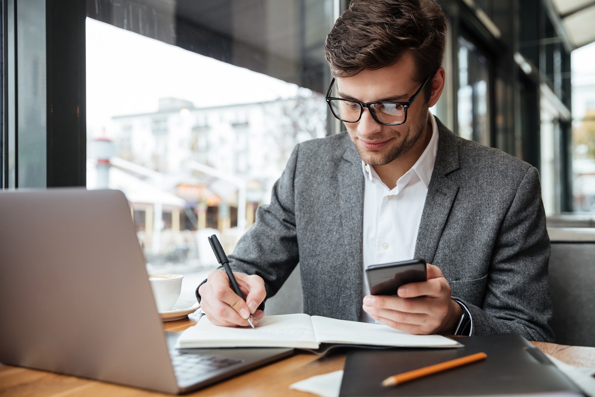 Smiling business man in eyeglasses sitting by table in cafe